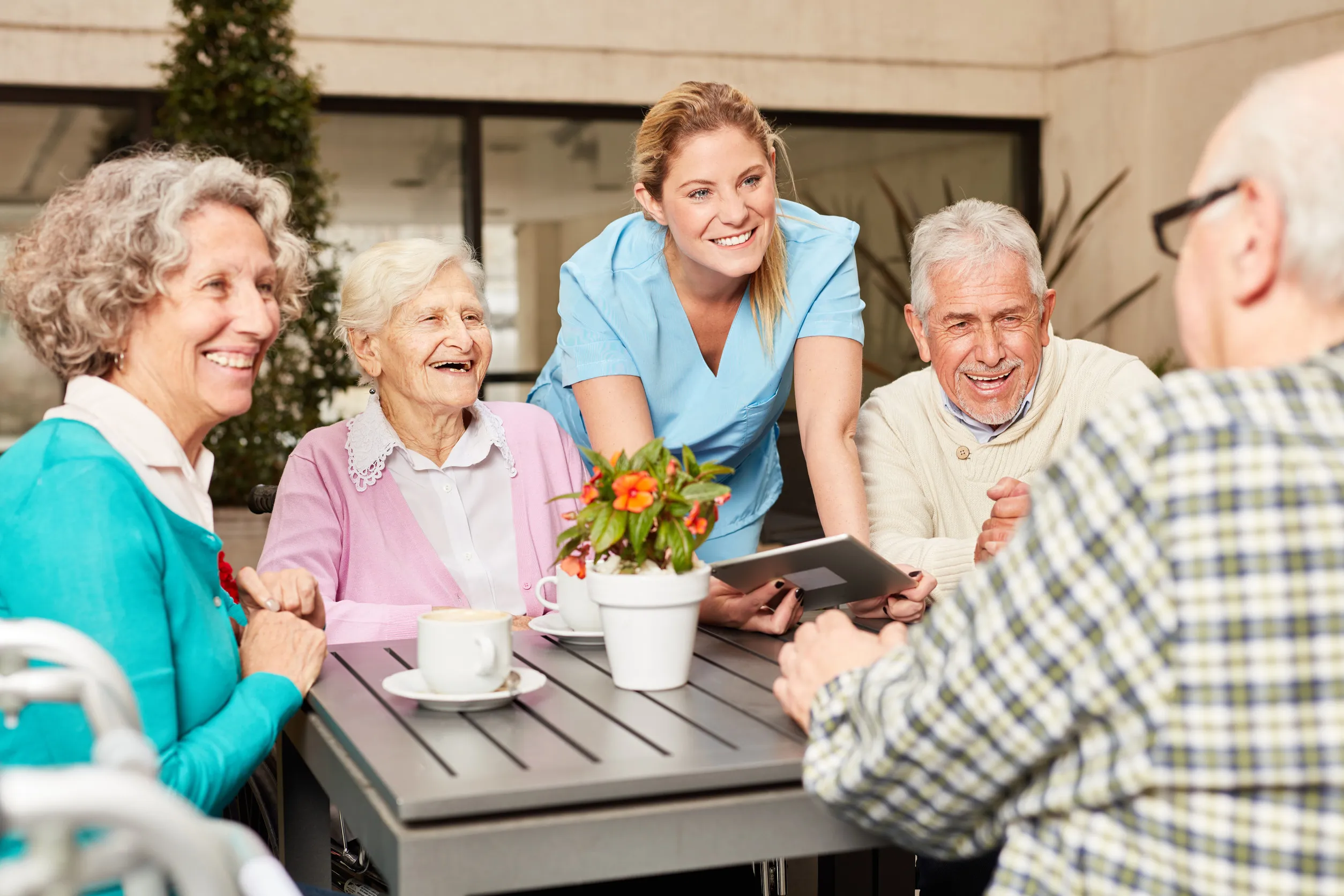 Group of seniors and caregiver using tablet computer while having coffee